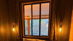 A bedroom with a large bed, two bedside lamps, a window with curtains, and a view of trees outside.