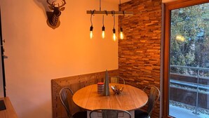 A dining area with a round wooden table, four chairs, a mounted deer head on the wall, and a large window with a view of trees.