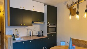 A modern kitchen with dark cabinets, a built-in oven, and a dining area with a round table and chairs.
