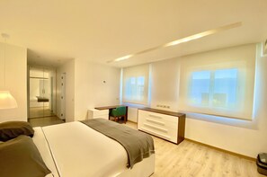 Habitación de hotel moderna con cama, escritorio y cómoda. Amplias ventanas ofrecen luz natural y vistas a la ciudad.
