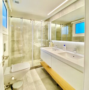 Un baño moderno con ducha de vidrio, un lavabo blanco con espejo y un inodoro.