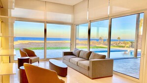 Een ruime woonkamer met een groot raam dat uitzicht geeft op het strand en het zwembad.