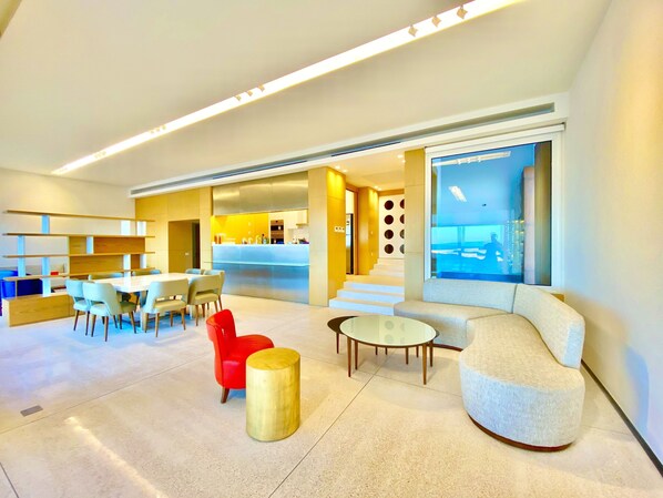 Un moderno vestíbulo de hotel con comedor, bar y zona de estar con un amplio ventanal que ofrece vistas.