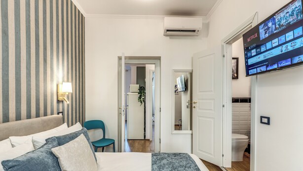 A hotel room with a bed, a TV mounted on the wall, and a door leading to a bathroom.
