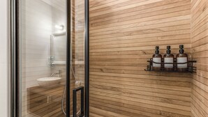 A modern bathroom with a wooden wall, a glass shower enclosure, and a shelf with three bottles.