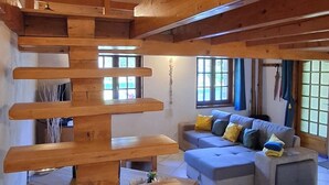 A wooden staircase leading to an upper floor, a grey sectional sofa with cushions, and a tiled floor. - Small vacation home for 4 people. (Banne)