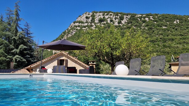 A swimming pool with a mountain backdrop, a stone building, and lounge chairs. - Small vacation home for 4 people. (Banne)