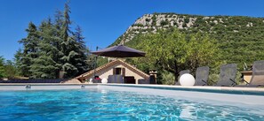 Une piscine avec une vue sur les montagnes, un bâtiment en pierre et des chaises longues.
