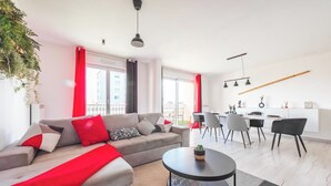 Ein modernes Wohnzimmer mit einer Couch, einem Esstisch und Stühlen. Es gibt eine Küchenzeile mit einer Bar und einer Pendelleuchte.