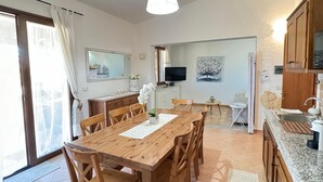 A spacious kitchen with a wooden table and chairs, a TV, and a dining area with a view of the outside. - Terraced house with swimming pool, surrounded by nature, 250 meters from the sea (Marina, Tertenia)