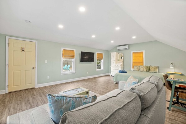 A spacious room with a large bed, a sofa, a desk, and a television on the wall.