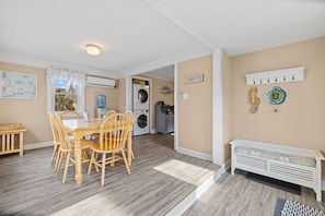 A dining area with a table and chairs, a washing machine, a bench, and a wall-mounted shelf with hooks. - Sandcastles & Sunsets: A Cape Cod Family Haven (Yarmouth)