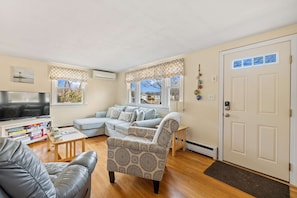 A living room with a sectional sofa, a patterned armchair, a flat-screen TV, and a bookshelf. - Sandcastles & Sunsets: A Cape Cod Family Haven (Yarmouth)