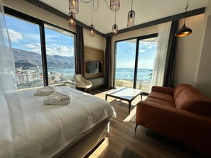 A hotel room with a bed, a sofa, a TV, and large windows offering a city and sea view. - Boreti Residence (Boreti)