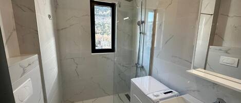 A modern bathroom with a glass-enclosed shower, a white toilet, a built-in sink, and a mirror above the sink.