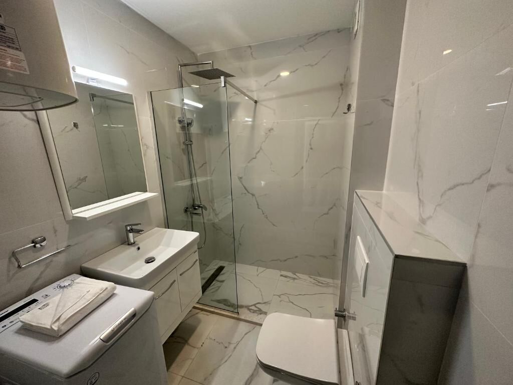 A modern bathroom with a glass-enclosed shower, a white sink, and a toilet.