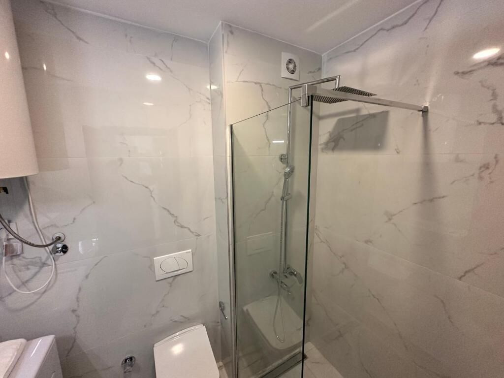 Een moderne badkamer met een douchecabine van glas, marmeren wanden en een wit toilet.