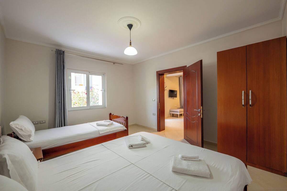 A hotel room with two beds, a wooden wardrobe, a television, and a bathroom visible through an open door.
