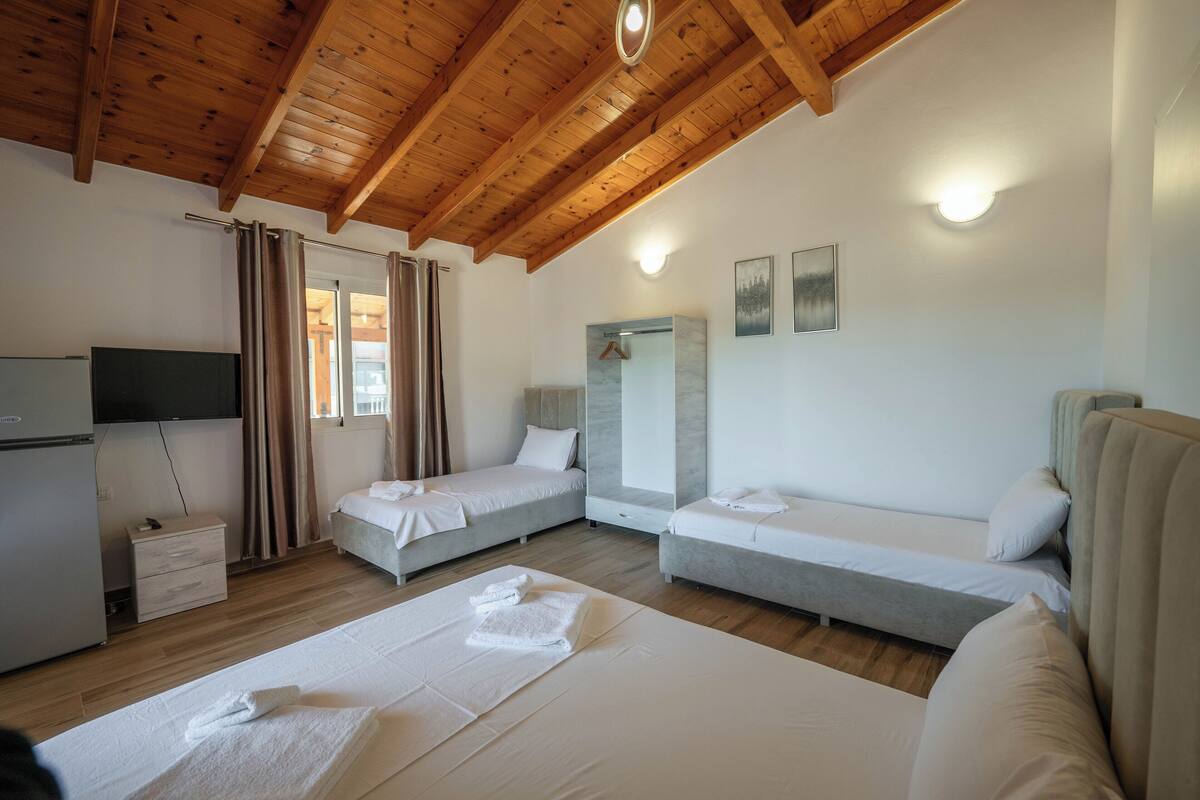 A hotel room with wooden beams, two single beds, a sofa, a TV, and a small desk.