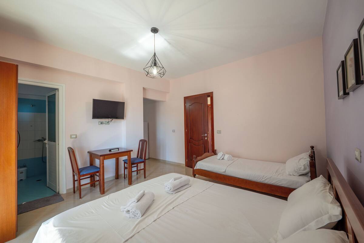 A hotel room with two beds, a desk, a chair, a TV, and a shower area.