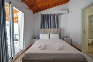 A bedroom with a large bed, two bedside tables, a headboard, and a sliding glass door leading to an outdoor area. - Sunny Villa (Ksamil)