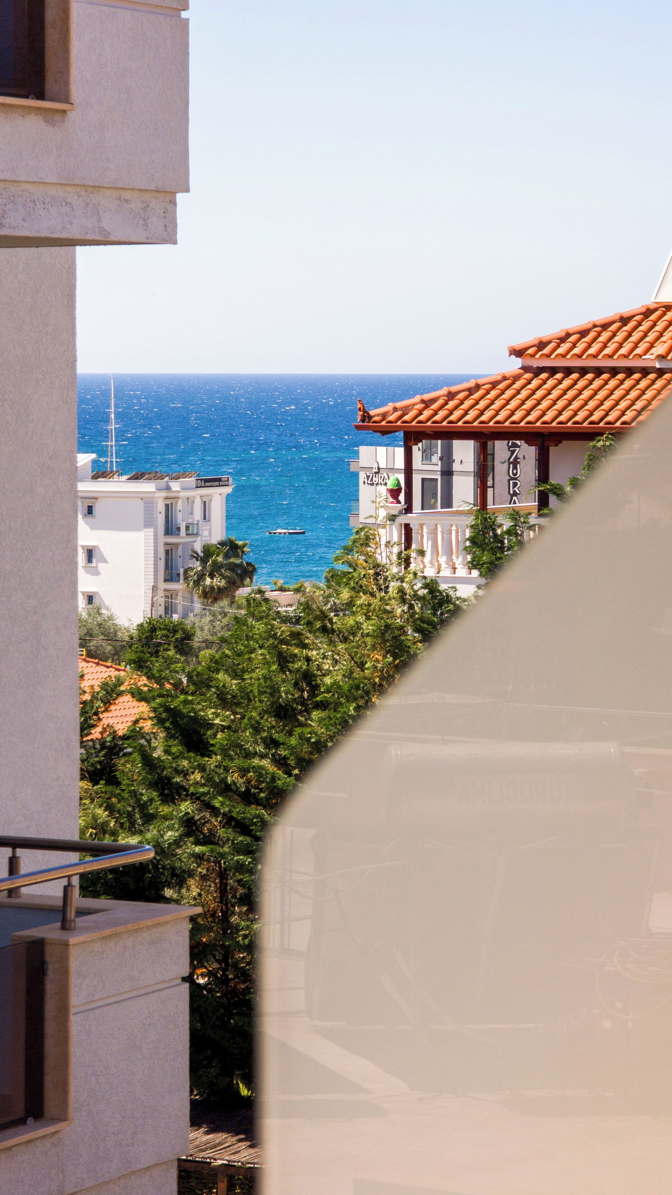 A coastal view with a building featuring a tiled roof and balconies overlooking the sea.