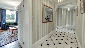 A hallway with striped wallpaper, a geometric patterned floor, and a mirror on the wall.