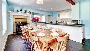 A spacious kitchen with a dining area set for six, featuring a central island, modern appliances, and a large window providing natural light.