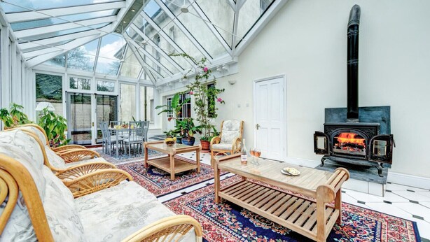 A conservatory with wicker furniture, a wooden coffee table, and a traditional wood-burning stove.