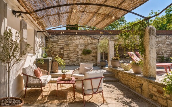 An outdoor patio with stone walls, wicker furniture, and potted plants.