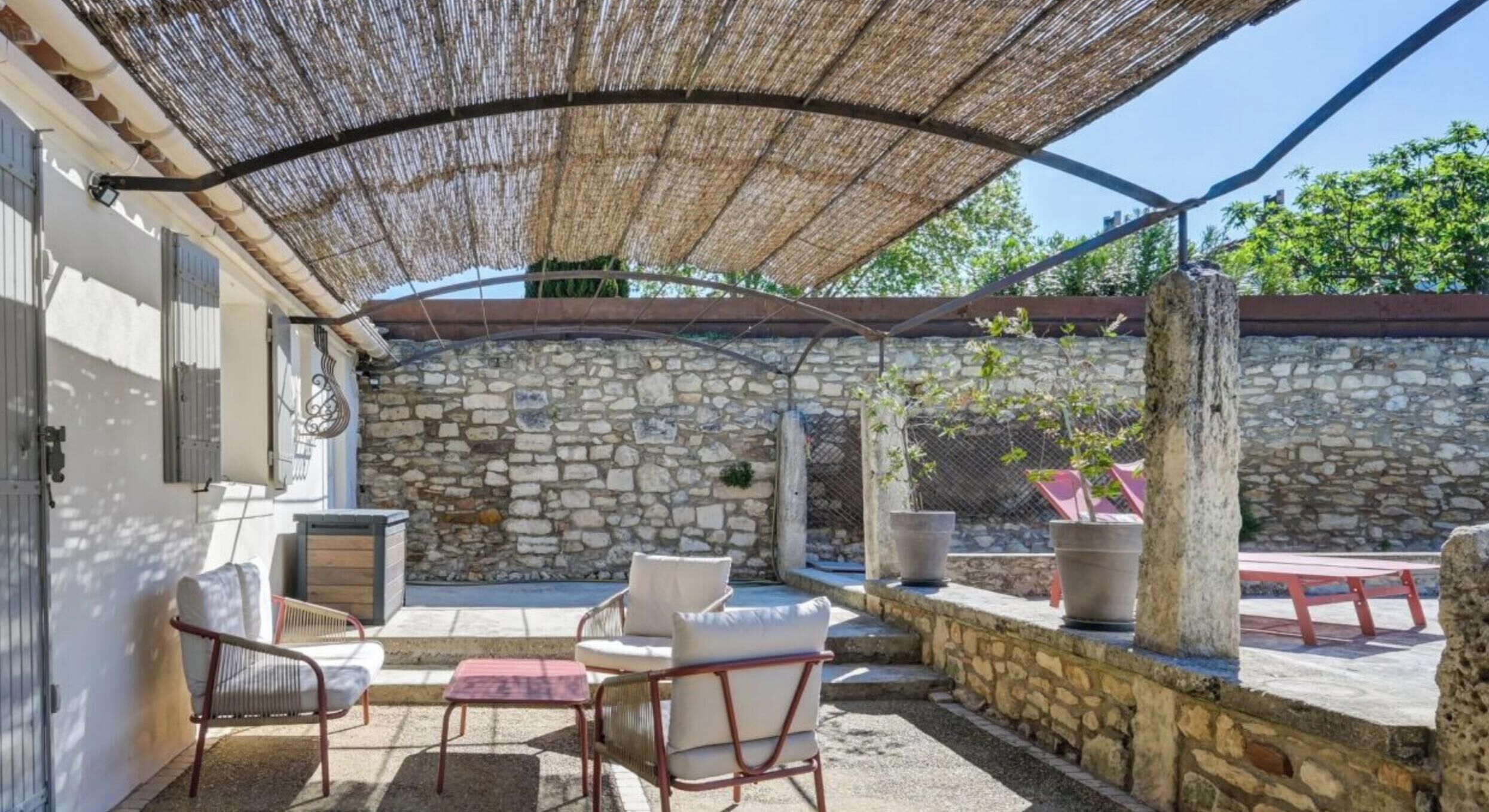 An outdoor patio with stone walls, a covered seating area, and potted plants.
