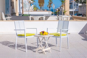 Une terrasse avec deux chaises blanches et une table, un saladier rempli de fruits et une vue sur la ville.