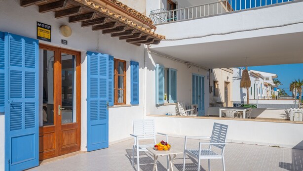 Exterior d'un hotel amb persianes blaves, un balcó i una taula amb fruita.