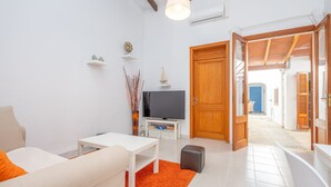 A modern living room with a white sofa, a small table, and a television on a white stand. There is a wooden door leading to another room. - Can Calpe in Mallorca (Santa Margalida)
