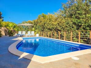 Piscina con cerco de madera, sillas de descanso y una pérgola.