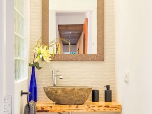 Un baño con lavamanos de piedra, un espejo y un florero con flores.