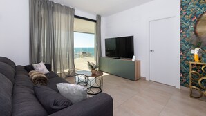A modern living room with a sofa, a coffee table, and a TV. There is a sliding glass door leading to a balcony with a view of the sea. - Bego a Sea View in Fuengirola (Fuengirola)