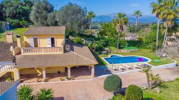 Casa de dos pisos con piscina, rodeada de palmeras y vista a las montañas.