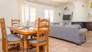 A dining area with a wooden table and chairs, a sofa, and a television in the background. - Casa Judith in Mallorca (Muro)