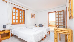 A hotel room with two beds, a wooden table, a chair, and a balcony with a view. - Casa Judith in Mallorca (Muro)