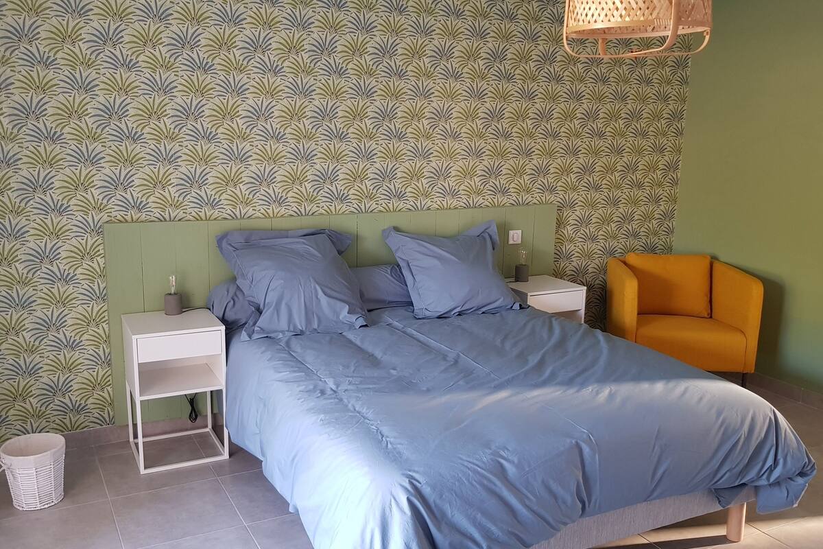 Een slaapkamer met een bed, nachtkastjes, een stoel, een muur met een bladpatroon en een hanglamp.