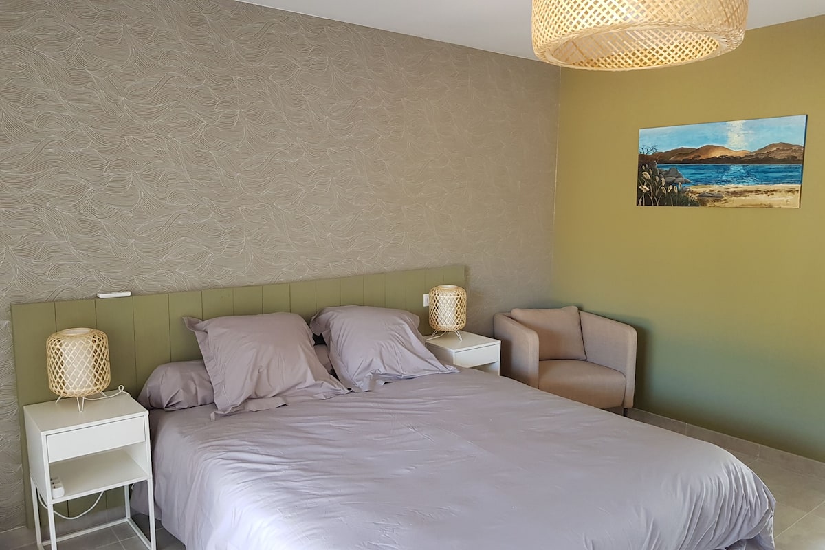 Een slaapkamer met een groot bed, twee nachtkastjes, een stoel, een lamp en een schilderij aan de muur.