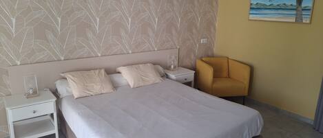 Un dormitorio con cama, mesitas de noche, una silla, un cuadro y una pared con diseño.