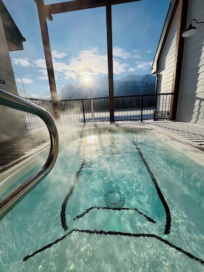 Une piscine aux eaux cristallines, dotée d’un plongeoir, d’une rambarde en métal et offrant une vue sur les montagnes en arrière-plan.