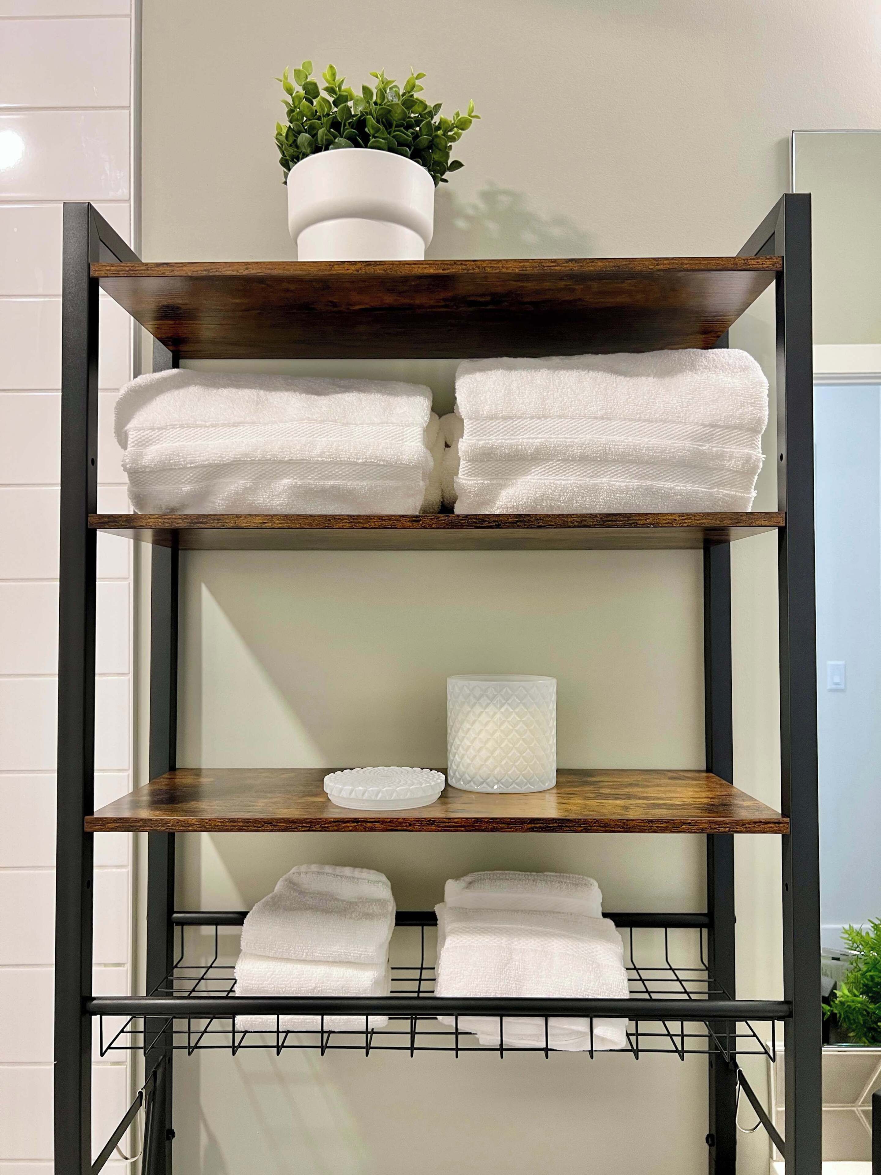 A metal shelf unit with multiple tiers, each holding folded white towels and a potted plant on the top tier.