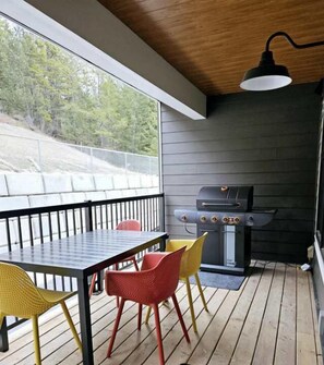 En täckt uteplats med ett bord och stolar, en grill och utsikt över omgivningen.