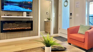 Una sala de estar moderna con un televisor de pantalla plana montado en una pared de madera, una chimenea abajo y un sofá naranja brillante con un cojín verde.