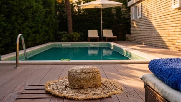 Ett trädäck med en pool, en halmhatt och solstolar.