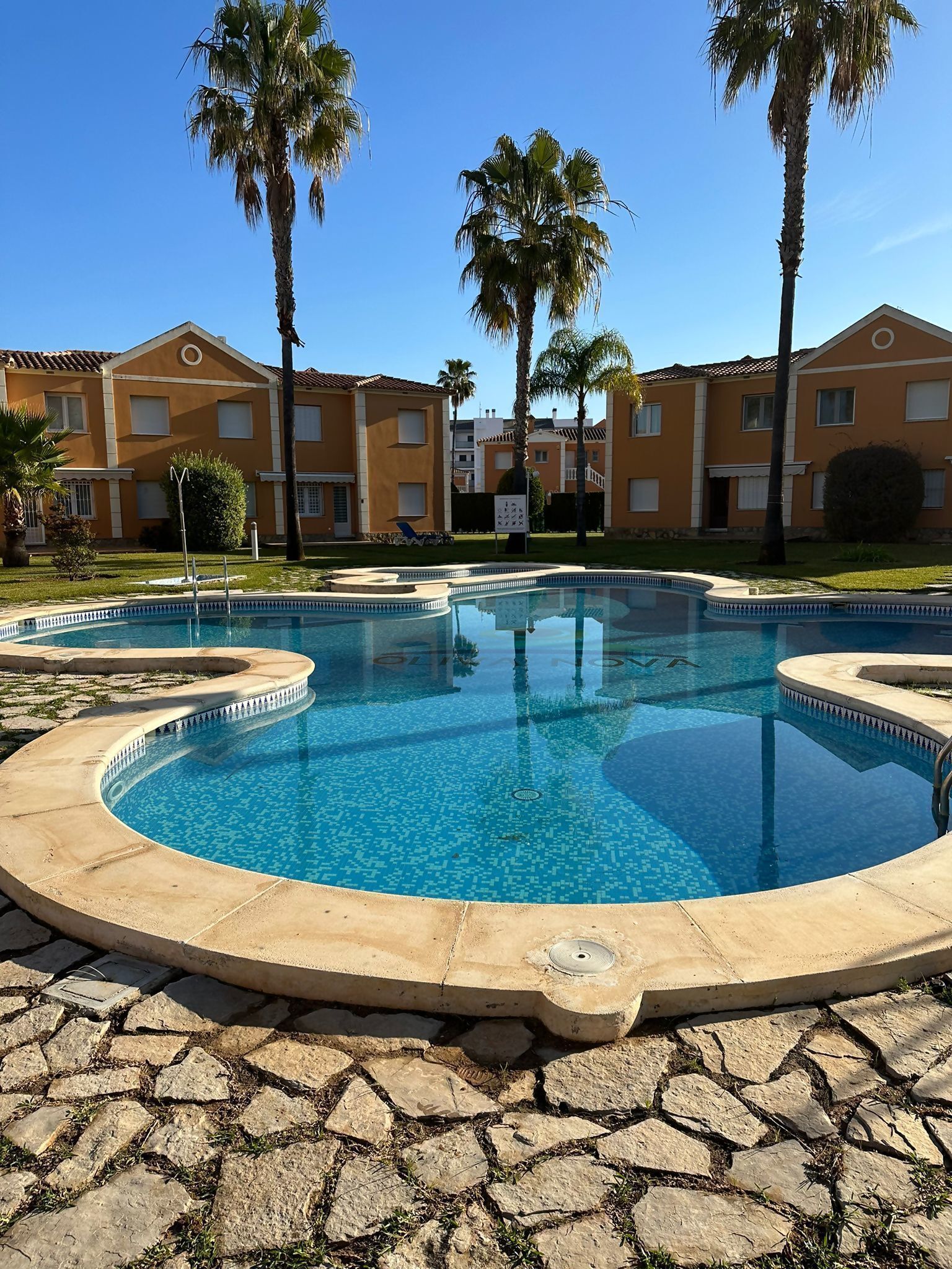 A swimming pool with a tiled edge, surrounded by a stone patio.