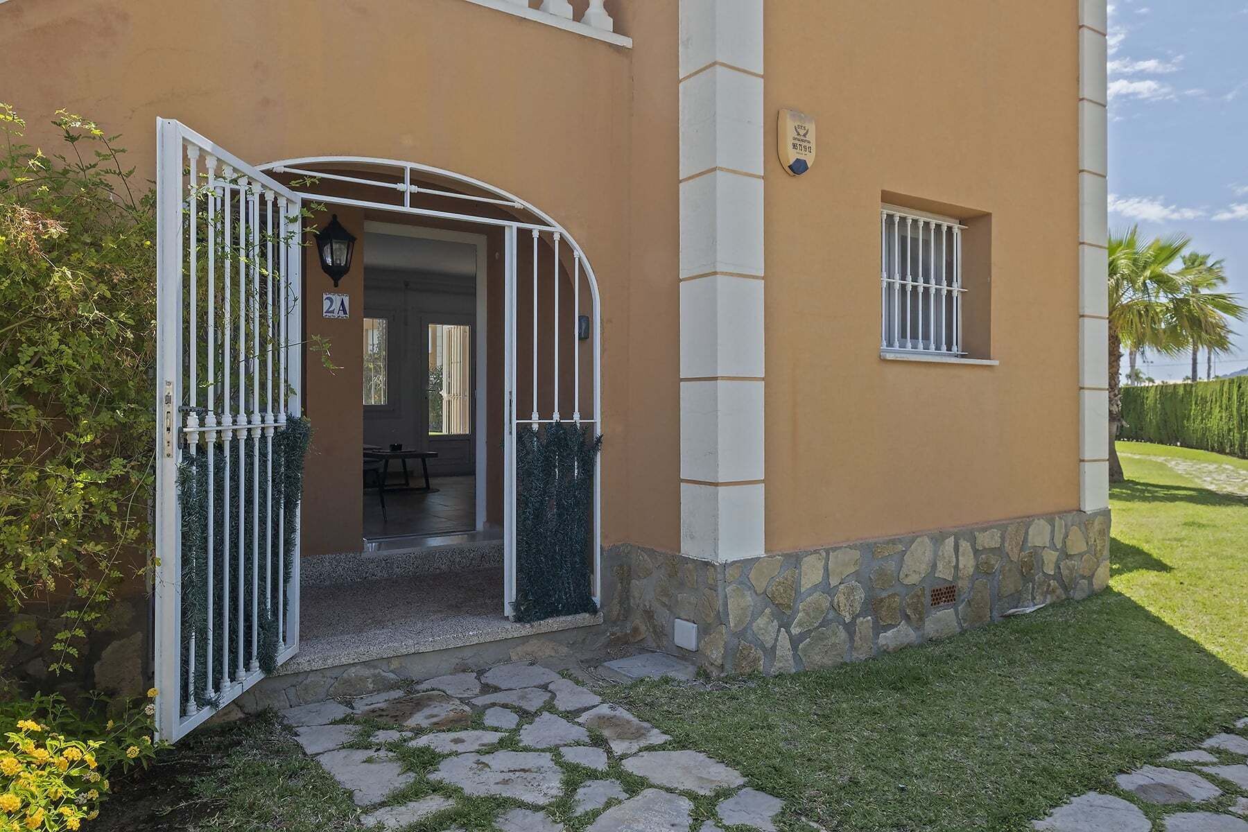 Una casa con cimientos de piedra, una puerta blanca con reja metálica y un ventanal pequeño con barrotes.